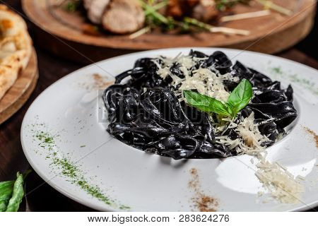 The Concept Of Italian Cuisine. Black Pasta With Cuttlefish Ink, Parmesan Cheese And Basil. Serving