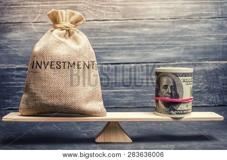 Money Bag With The Word Investments And Dollars On Scales. Attraction Of Financial Resources For Inv