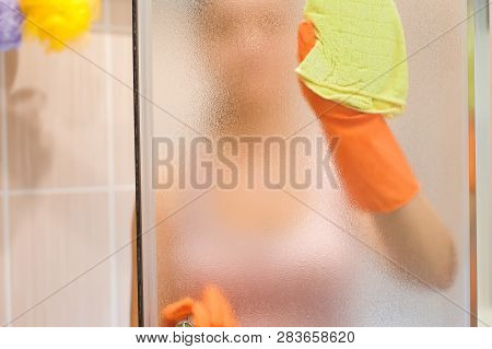 Young Woman Cleaning Shower Doorin A Bathroom