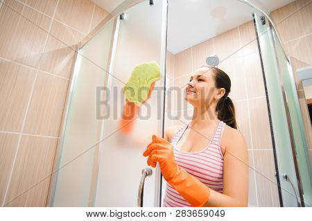 Young Woman Cleaning Shower Doorin A Bathroom