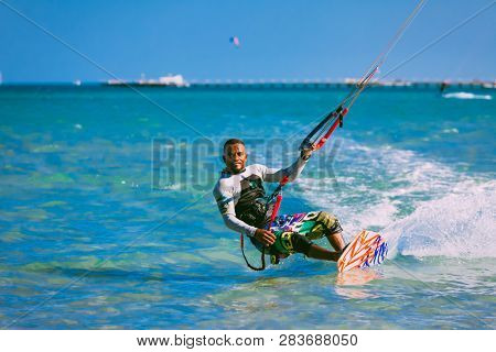 Egypt, Hurghada - 30 November, 2017: The kiter on the wakeboard holding the kite straps. The wave riding over the crystal clear Red sea surface. The professional kitesurfing. Extreme sport activity.