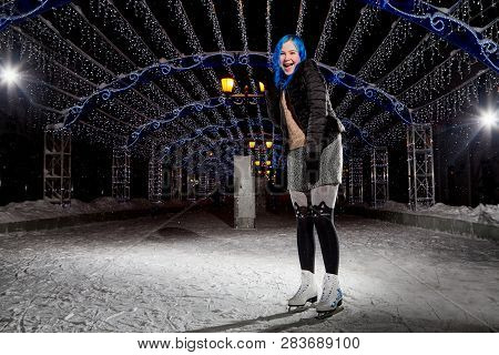Girl With Blut Hair Skating On The Ice Arena In The Evening City Square In Winter