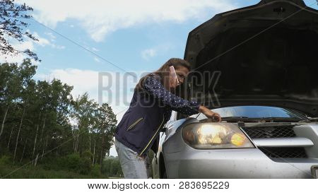 Young Brown-haired Woman Talking On Phone And Explaining Emotionaly Near The Hood Of A Broken Car