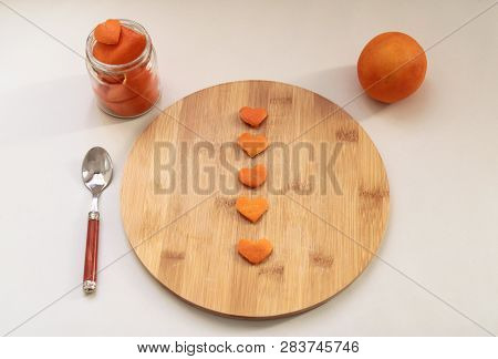 Heart-shaped Orange Peels On The Chopping Board Surrounded By The Orange, Spoon And Small Vase With 