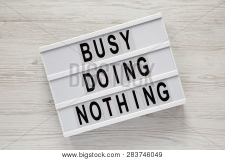 Modern Board With Text 'busy Doing Nothing' On A White Wooden Surface, Top View. From Above, Flat La