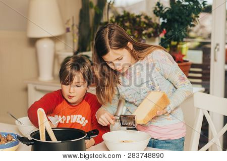 Two Kids Having Spaghetti Lunch At Home, Girl Sprinkling Pasta With Big Piece Of Cheese