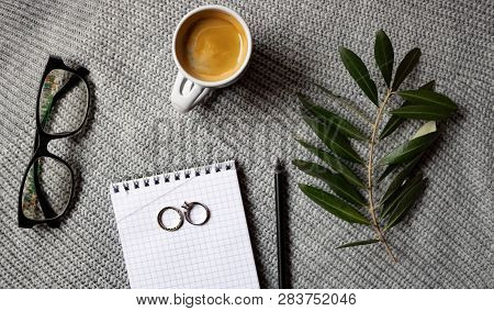 Coffee Cup, Olive Branch, Glasses, Notepad And Pencil On The Gray Sweater Background