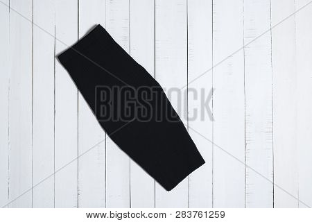 Clothes And Accessories. Black Midi Skirt On White Wooden Floor Planks. Flat Lay.