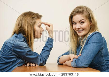 Woman Saying Bad Things About Her Over Confient Female Friend. Pointing At Forehead, Stupidity Gestu