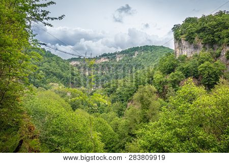 Skybridge Suspension Bridge Over A Precipice On A Cloudy Day. Green Forest Around. Skypark, Sochi, R
