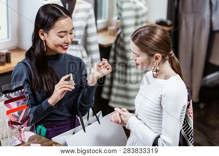 Smiling Pretty Long-haired Woman In A White Sweater Smelling A Fragrance