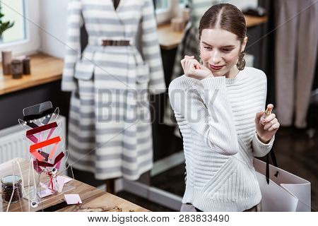 Smiling Pretty Long-haired Woman In A White Sweater Looking At The Bottles With Fragrances
