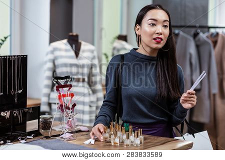 Dark-haired Smiling Asian Lady In A Dark-blue Blouse Testing Fragrances