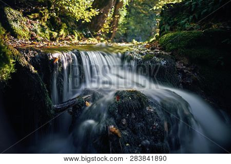Long Exposure Of A River Creek With A Small Waterfall. Sunset And Strong Detail Bokeh View. Blue Cal