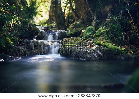 Long Exposure Of A River Creek With A Small Waterfall. Sunset And Strong Detail Bokeh View. Blue Cal