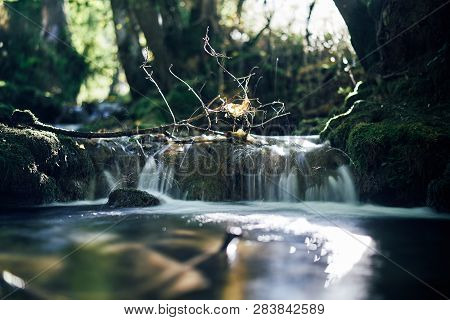 Long Exposure Of A River Creek With A Small Waterfall. Sunset And Strong Detail Bokeh View. Blue Cal