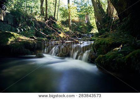 Long Exposure Of A River Creek With A Small Waterfall. Sunset And Strong Detail Bokeh View. Blue Cal