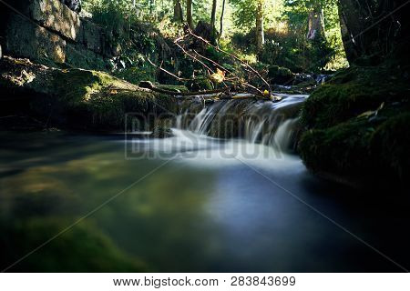 Long Exposure Of A River Creek With A Small Waterfall. Sunset And Strong Detail Bokeh View. Blue Cal