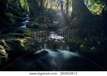Long Exposure Of A River Creek With A Small Waterfall. Sunset And Strong Detail Bokeh View. Blue Cal