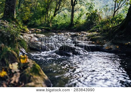A River Creek With A Small Waterfall. Sunset And Strong Detail Bokeh View. Blue Calm Warm Water