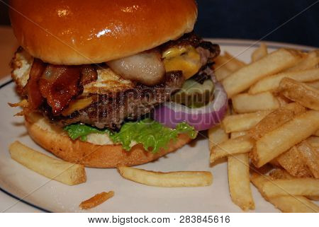 A Loaded Cheeseburger Emplated Messily With French Fries.