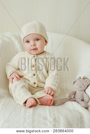 Sweet Baby Wearing Knitted Suit Is Sitting On The Chair