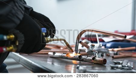 Worker Is Soldering A Pipe By A Blow Lamp On A Factory Workbench Background. Pipework.