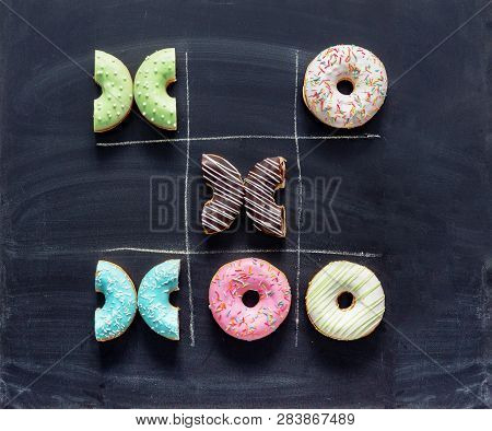 Tic Tac Toe Made Of Donuts. Game Noughts And Crosses With Donuts On Chalkboard. Unhealthy Diet, Diab