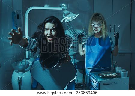 Horror Scene In Dentist Office. Crazy Evil Stomatologist Treating Teeth To Scared Patient In Dental 