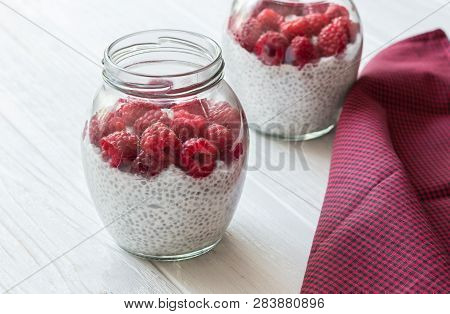 Glass Jars Of Pudding From Chia Seeds With Coconut Milk And Raspberry Berries In White Wooden Table 