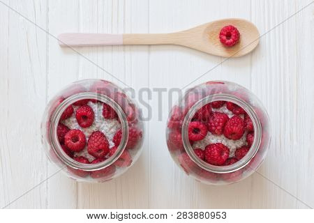 Glass Jars Of Pudding From Chia Seeds With Coconut Milk And Raspberry. Wooden Spoon With Berry In Wh