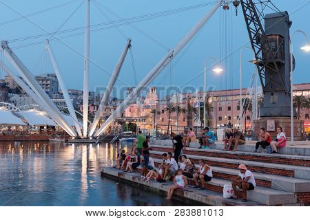 GENOA, ITALY - AUGUST 5, 2018: People resting at sea in the old port, Porto Antico in a summer evening. The panoramic lift Bigo offered a full view of the harbor and city, is visible on the back left