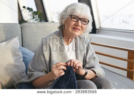 Picture Of Neat Retired Woman Wearing Wide Scarf And Eyeglasses Knitting Warm Jumper For Her Daughte