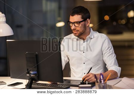 business, design and technology concept - creative man or designer in glasses with computer and pen tablet working at dark night office