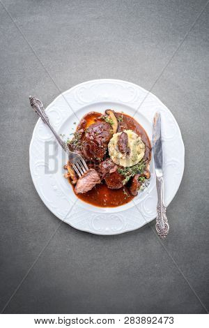 Traditional German braised pork cheeks in brown red wine sauce with mushroom and mashed potatoes as top view on a classic design white plate with copy space 