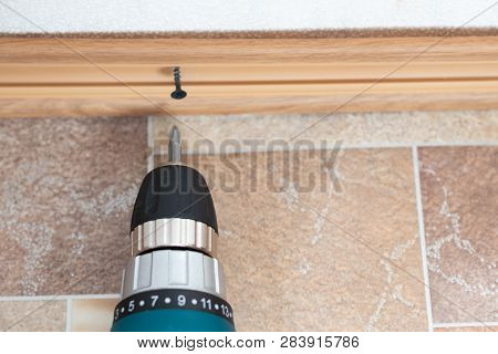 Installation Of Plastic Floor Plinth. Interior Details. Worker With A Screwdriver In His Hands Mount