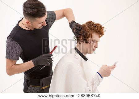 Side View Of Concentrating Barber Holding A Comb And Scissor Deciding What Haircut To Make. Ginger M