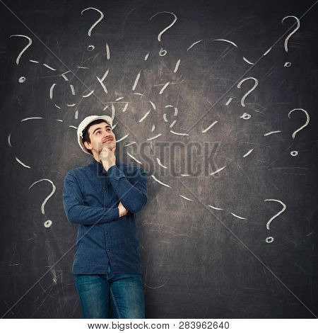Positive Young Man Engineer Wearing Protective Helmet Holding Hand Under Chin Looking Up Thoughtfull