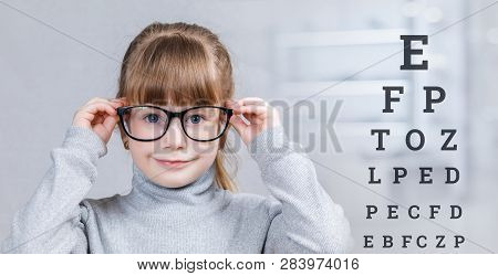 A Smiling Child In Glasses Is Standing With Checking Table With Letters Behind Her At The Blurred Me