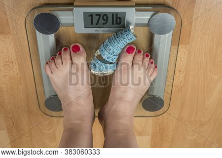 A Woman Stands With Two Feet On A Scale. Overweight Concept