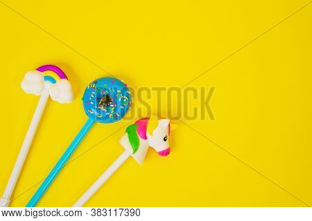 Colorful Pencils With Erasers In The Form Of Donut, Unicorn And Rainbow On Clouds, Yellow Background