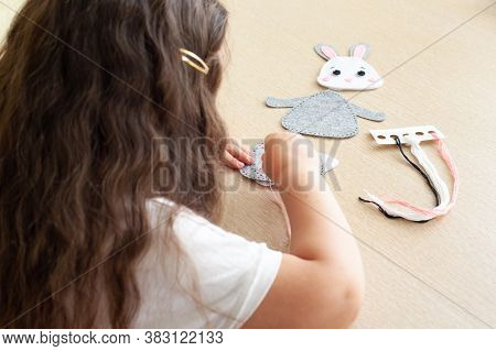 Child Girl Sews A Toy Made Of Felt Sitting At The Table.
