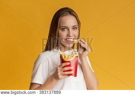 Harmful Food. Portrait Of Happy Young Woman Eating French Fries Potatoes And Looking At Camera, Posi