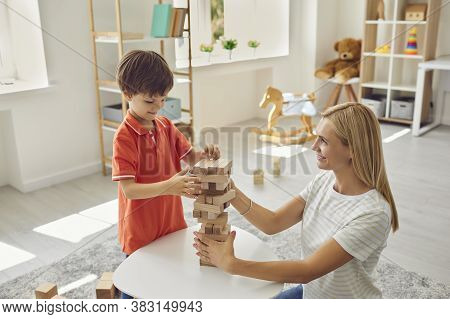 Happy Mother Shelping Smiling Son To Build Wooden Pyramid Of Parts At Home