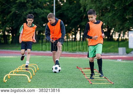 Active Teen Footballers Train Together On Artificial Soccer Field And Follow The Instructions Of A P