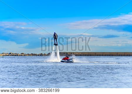 Man Having Fun On Flyboard. Flyboarding In A Sunny Summer Day At River In Harbor. Extrime Water Acti
