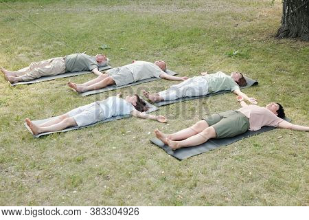 Group of mature yoga students lying in corpse pose on mats while resting after training in park