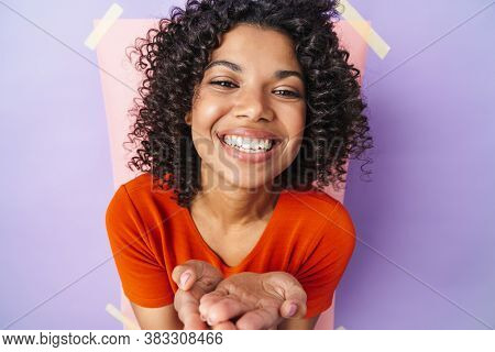 Image of funny african american woman smiling and holding copspace isolated over multicolored background