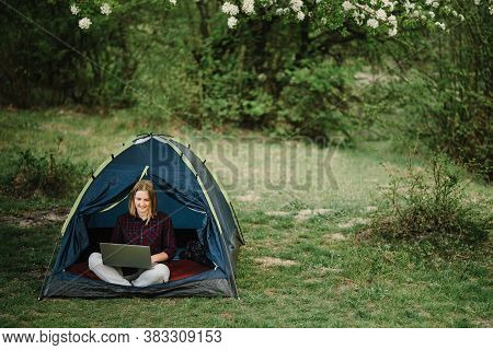Woman Working On Laptop In Tent In Nature. Young Freelancer Sitting In Camp. Relaxing In Camping Sit
