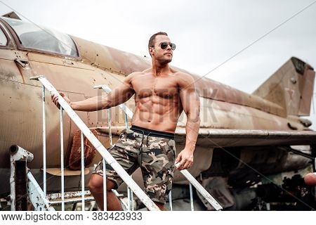 An Attractive Sportsman In Brutal Soldier Fashion. Abandoned Stationary Airplane In Old Airport And 